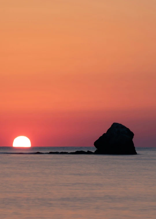 a large rock sticking out from the ocean as the sun sets