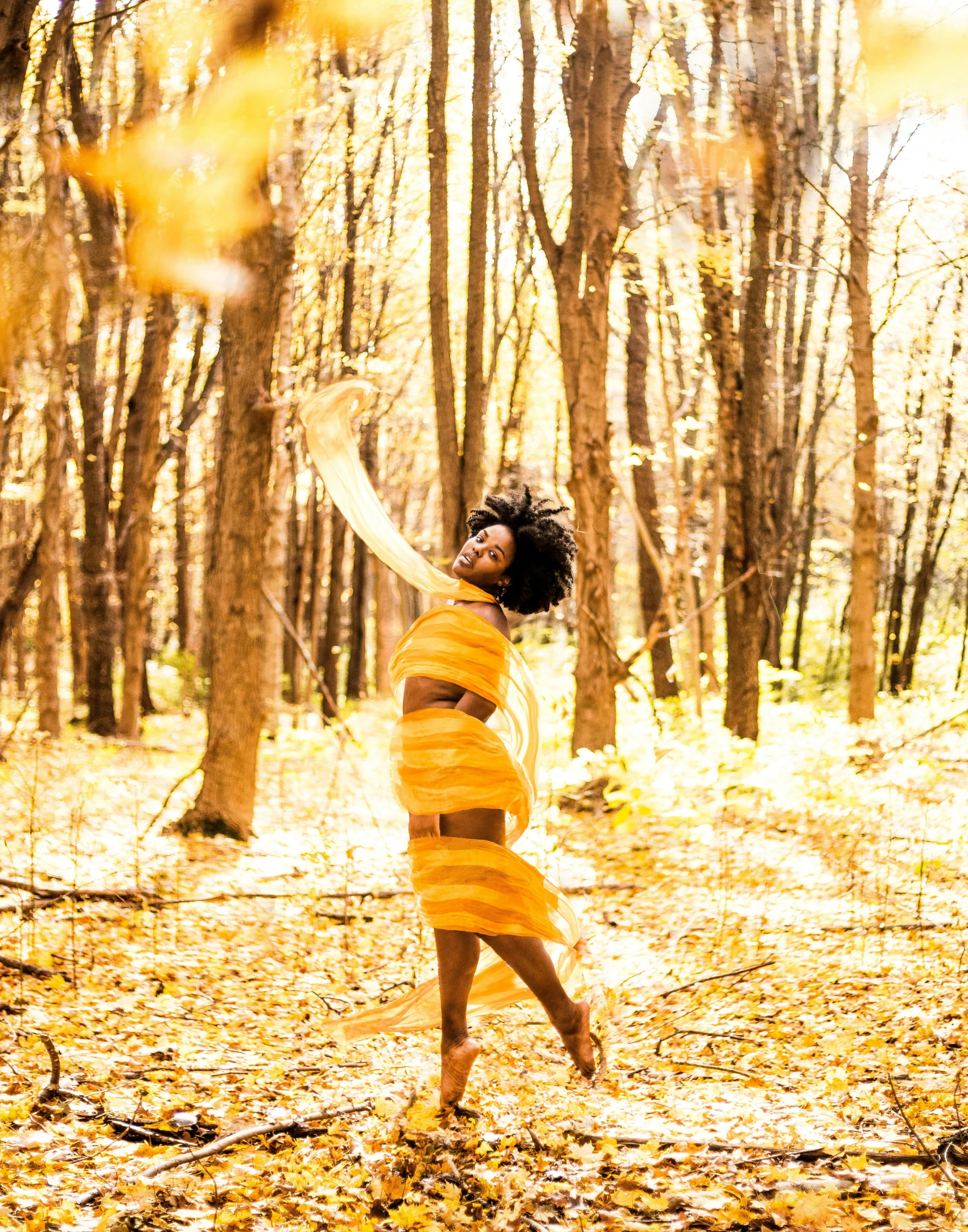 an attractive woman stands in the woods in front of trees with a frisbee