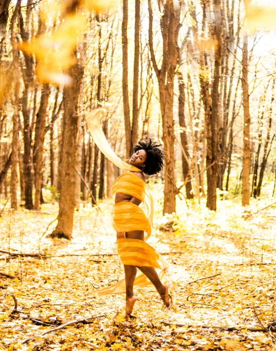 an attractive woman stands in the woods in front of trees with a frisbee