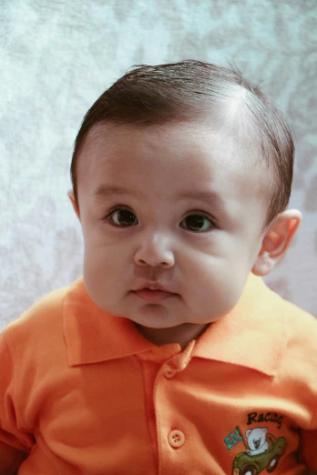 a small boy with short hair is wearing an orange shirt