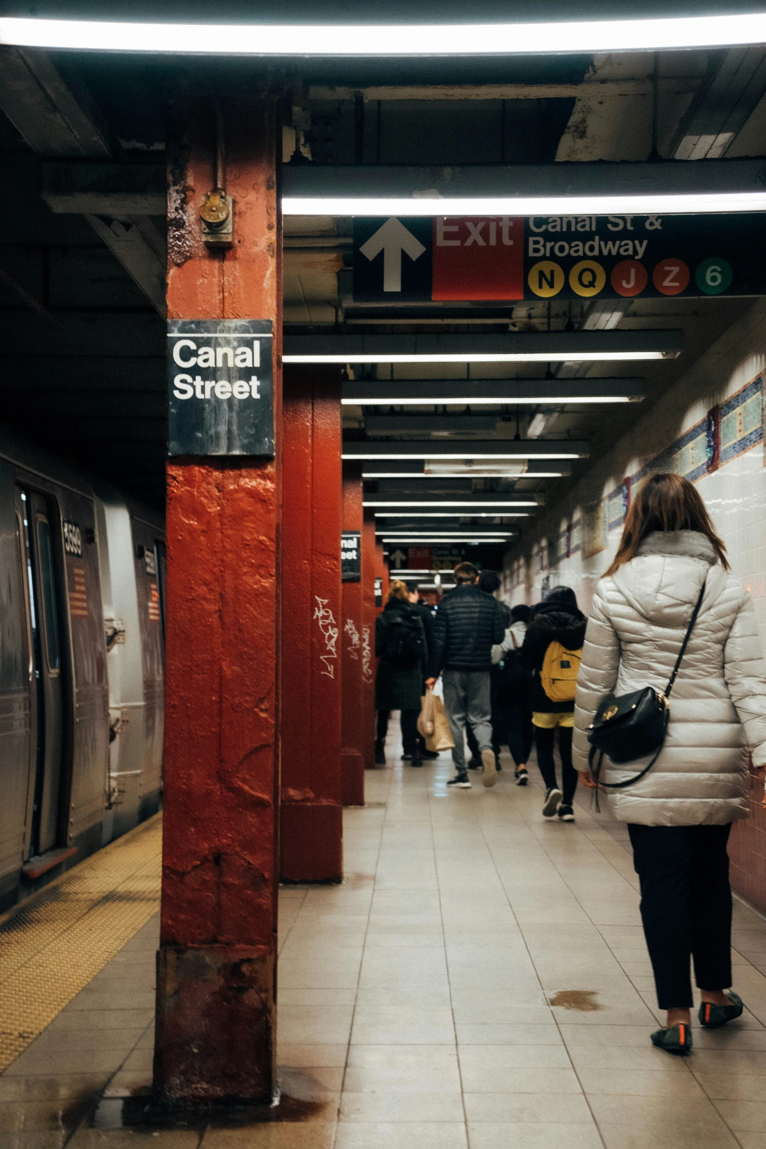 people walk along a subway platform as the train stops