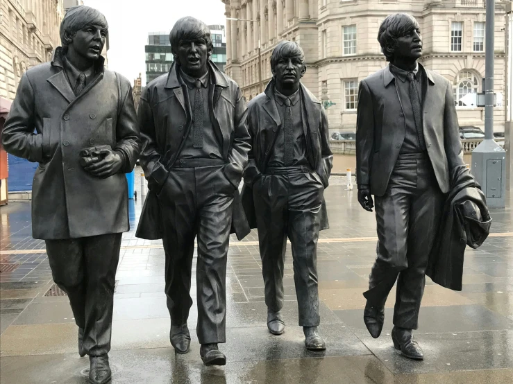 four statues stand in the rain with one facing away from camera