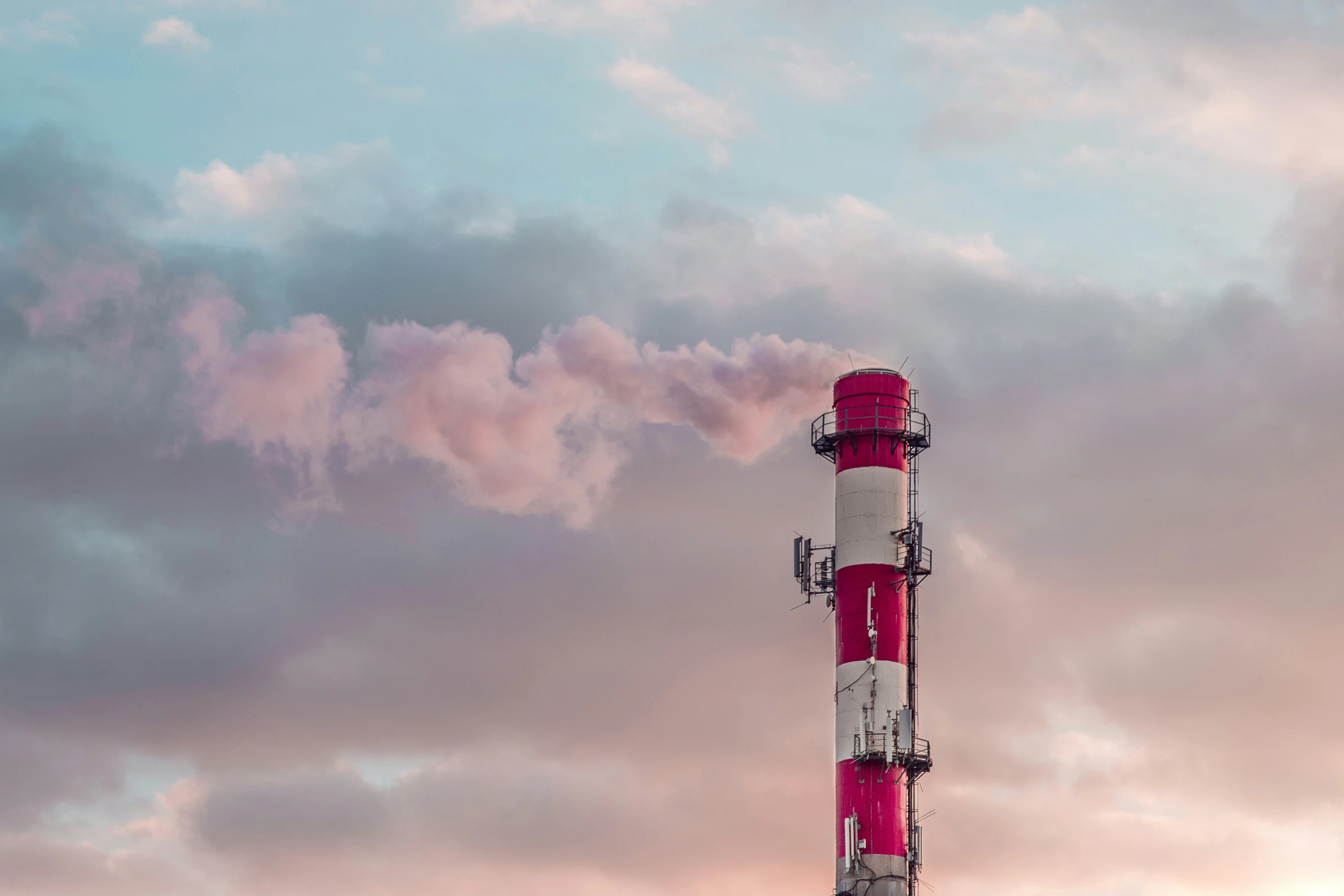 factory smoke billows from the top of a tall red and white structure