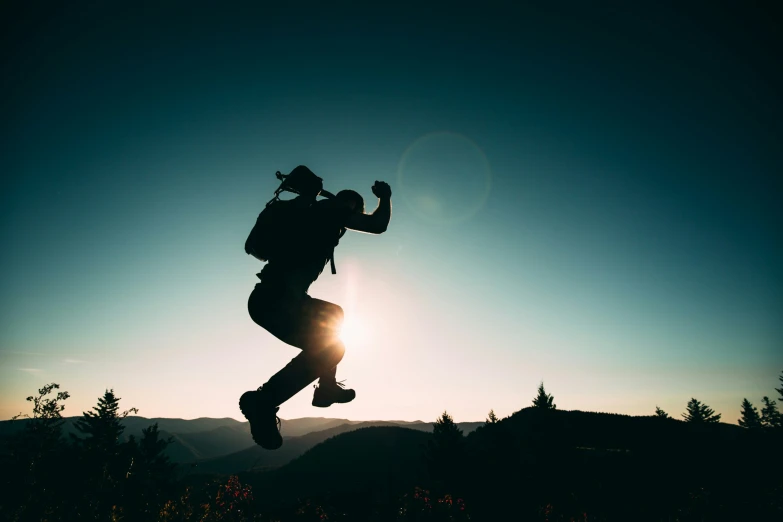 a person jumping in the air above trees at sunset