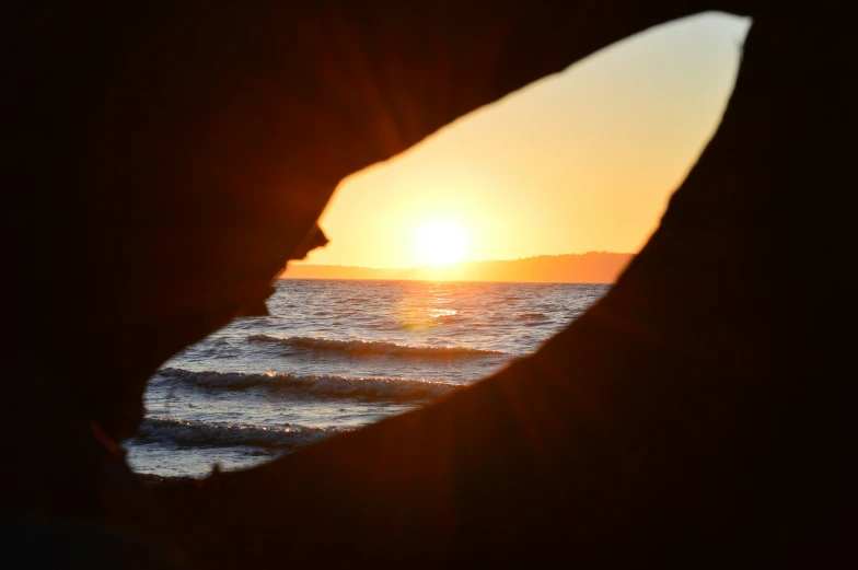 the sun shines through two silhouetted hands as they stand on a wave, with the water in the background