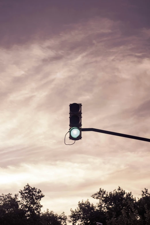 a stoplight suspended over trees with a sky background