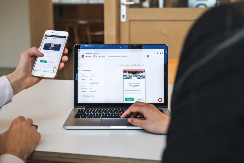 two people are at the table in front of a laptop and phone