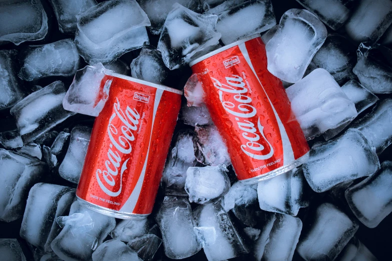 two cans of coke are sitting on an ice slab