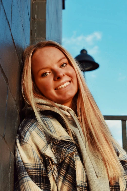 a smiling woman stands in front of a brick wall