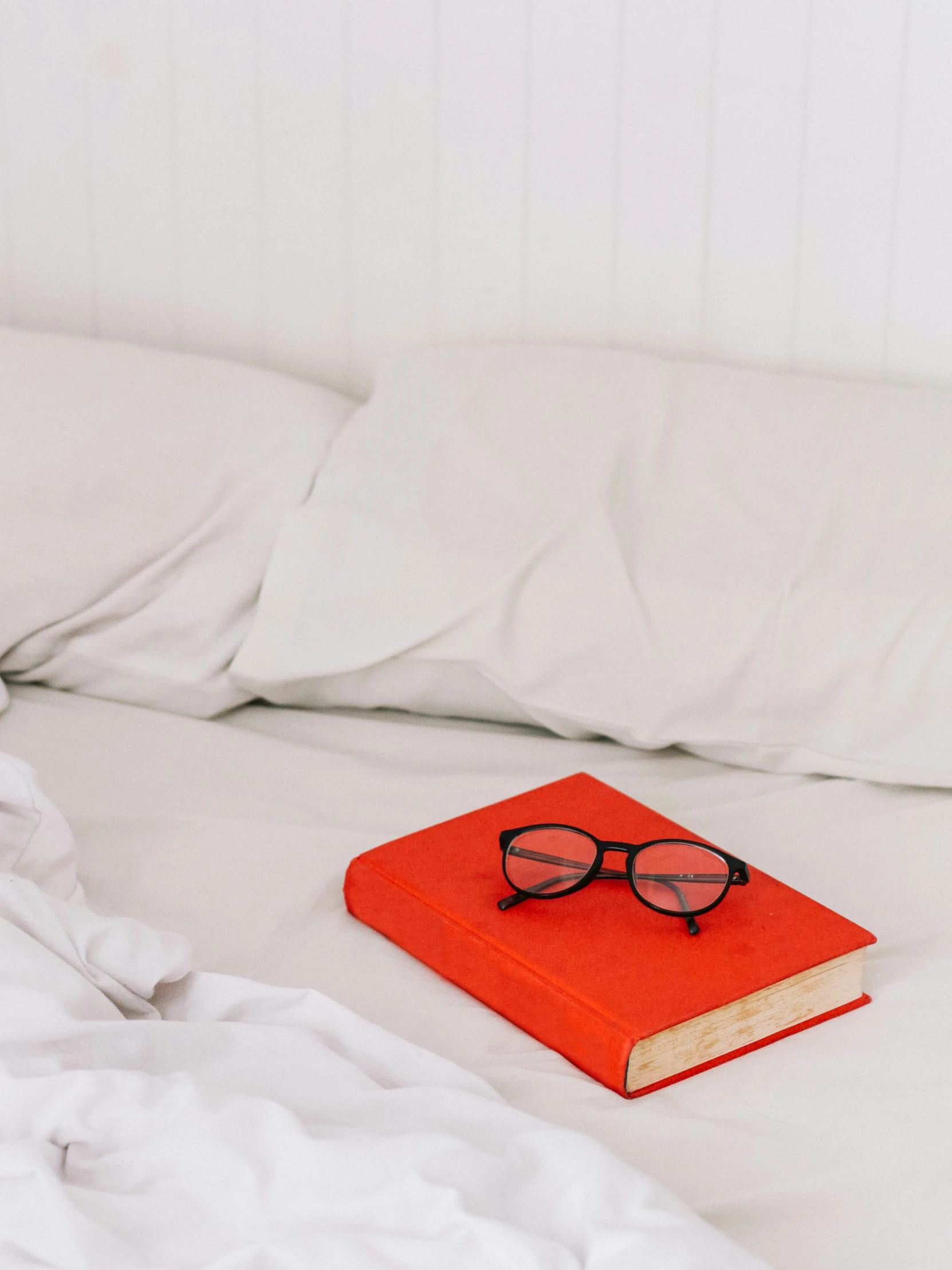 a book, pair of glasses, and white sheets on a bed