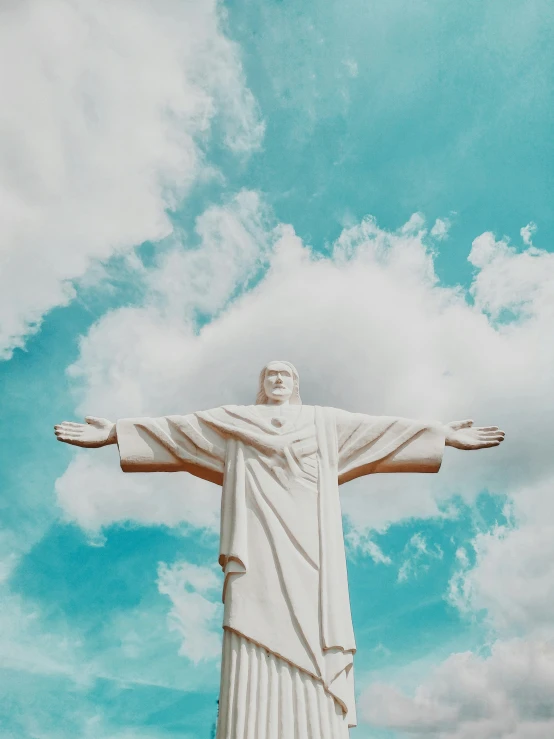 the statue of christ is soaring in a cloudy blue sky