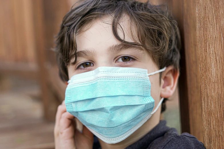 a boy wearing a surgical mask with a wooden wall behind him