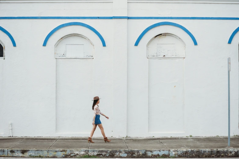 a woman walking across a street past white building