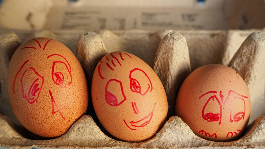 three egg shells with painted faces in an egg box