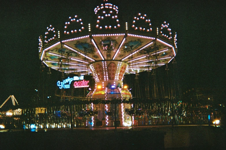 a fairground is lit up at night with lights on the carousel