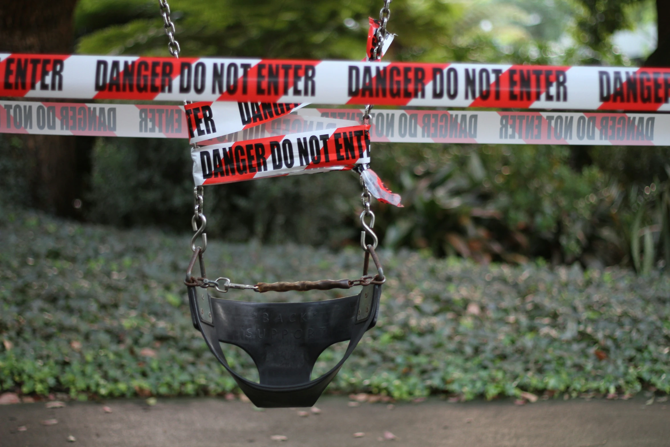 a broken swing sitting near a barricade with warning tapes