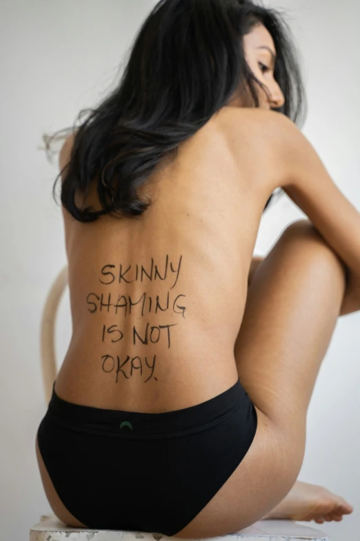 a woman with a tattoo saying skinny is standing is not okay