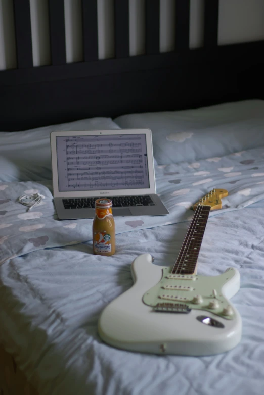 a white guitar is laying on a bed next to a bottle of beer