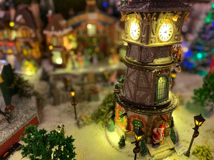 a lite up clock tower in front of a model village