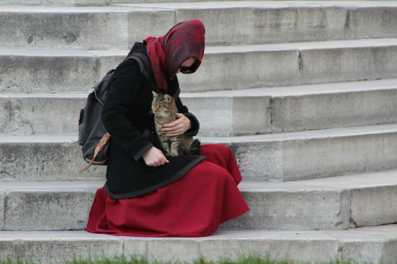 a woman is sitting on the steps petting a cat