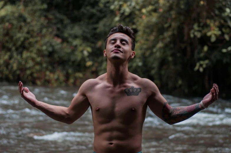 shirtless man with arm raised next to a small stream