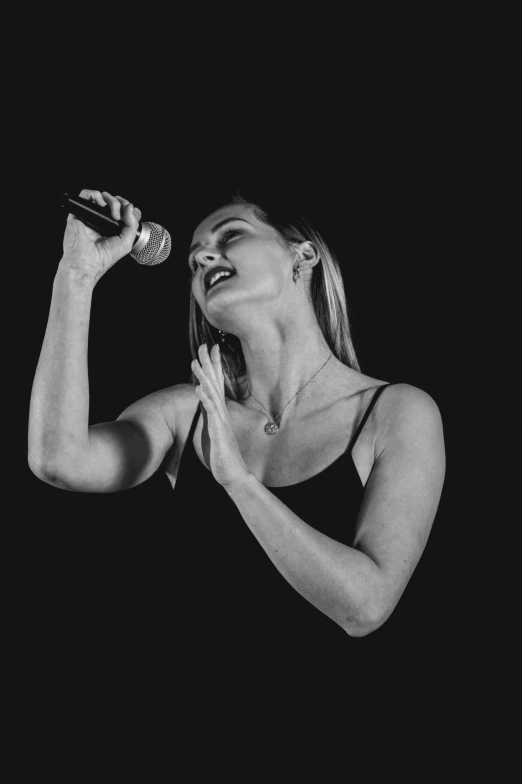 woman with blonde hair wearing black dress singing into a microphone