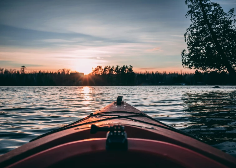 a view from the bow of a red canoe looking towards a setting sun