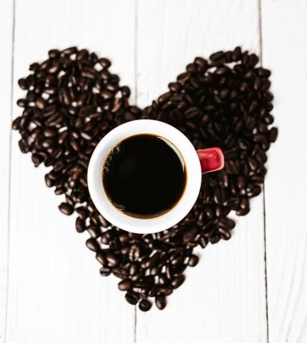 a heart - shaped cup sits between two coffee beans