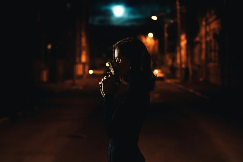 a woman standing on a dark street holding her cigarette