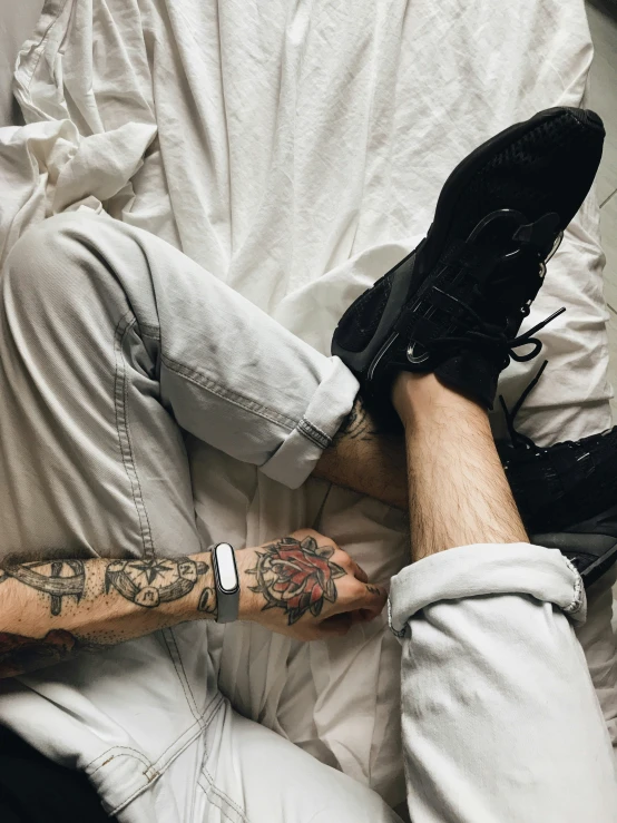 man in black sneakers resting on a bed covered with sheet