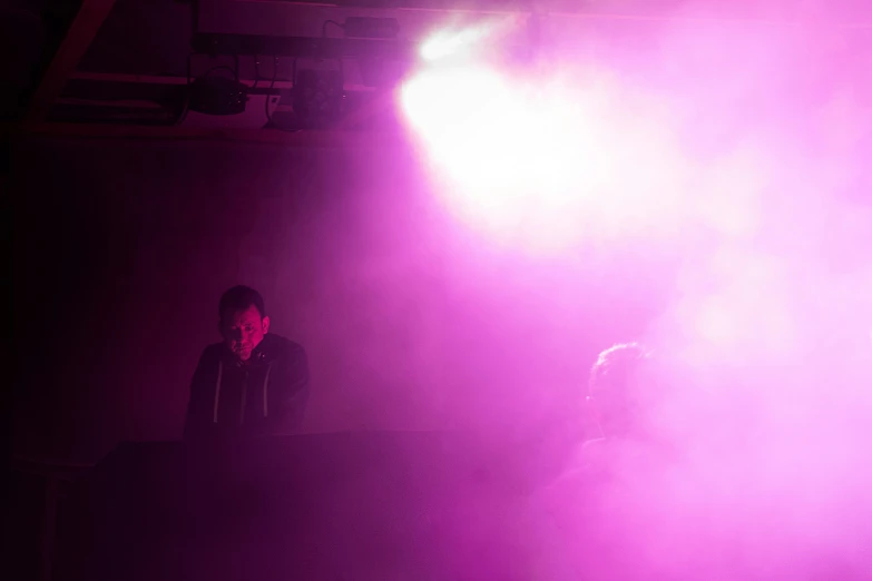 two people sitting on a stage and one standing in front of a purple light