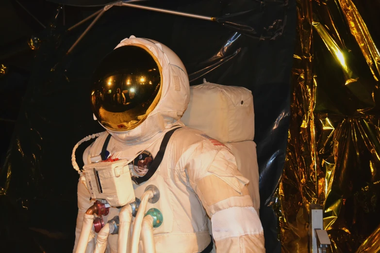 a spaceman standing next to a tall, shiny golden balloon