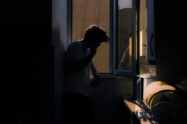 a man standing next to an open window talking on a phone