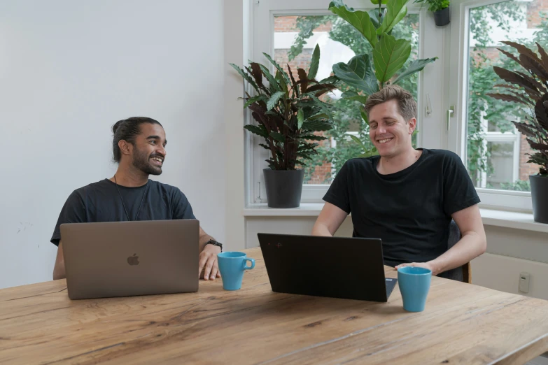 two men sitting at a table with laptops in front of them