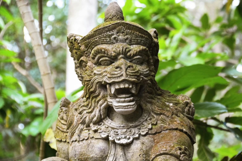 a statue with a demon face sits next to a tree