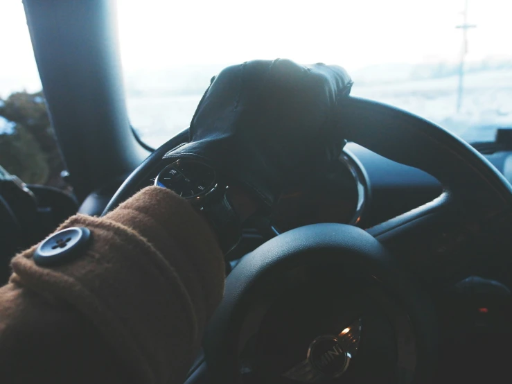 person in glove steering a car with sun light reflecting on dashboard