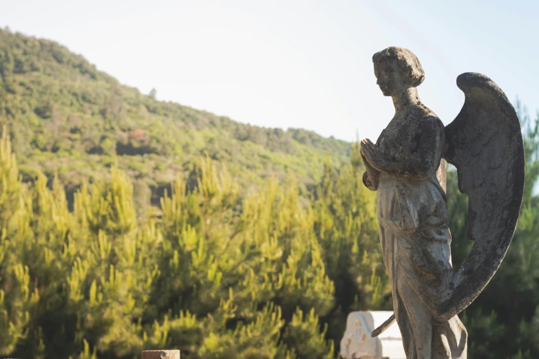 an angel statue stands near a hill and green trees