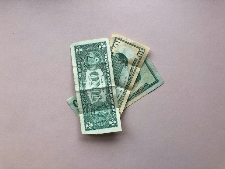 a group of five dollars on top of a pink surface