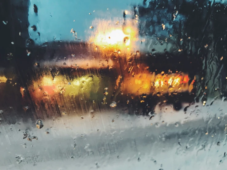 rain pouring on the window while street lights sit in front