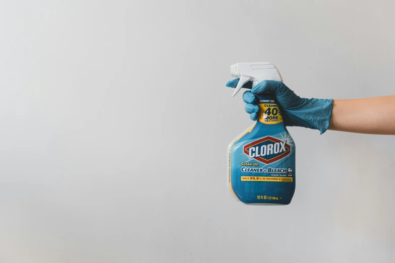 a hand wearing gloves and blue rubber glove holding up a bottle of clorox cleaner