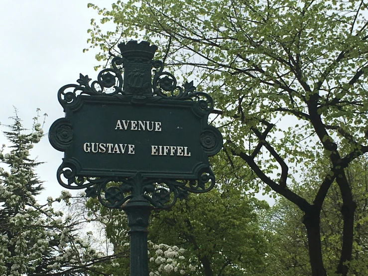 a black street sign on top of a post next to trees