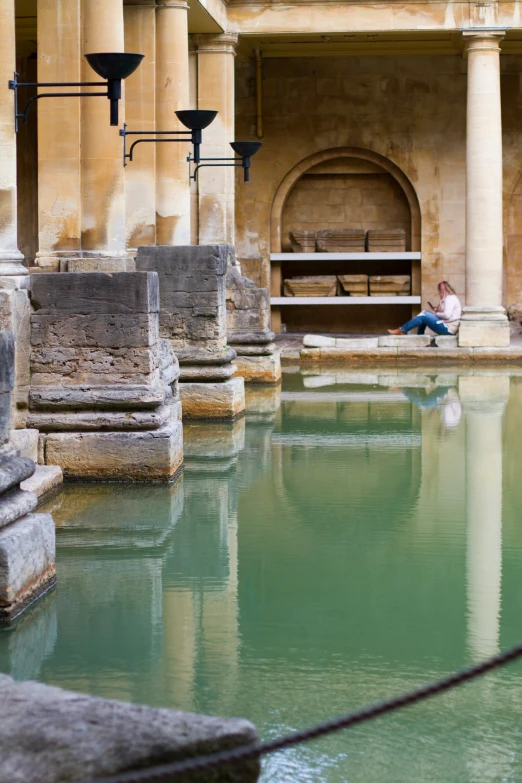 two girls sit on the bank of a fountain in a stone building