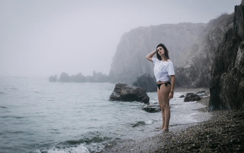 a woman is standing on the shore by a rocky beach