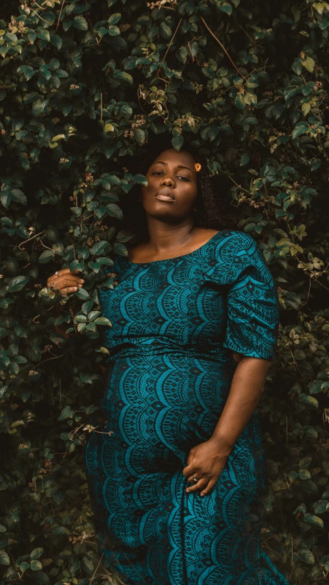 woman wearing blue with large arms standing in front of bushes