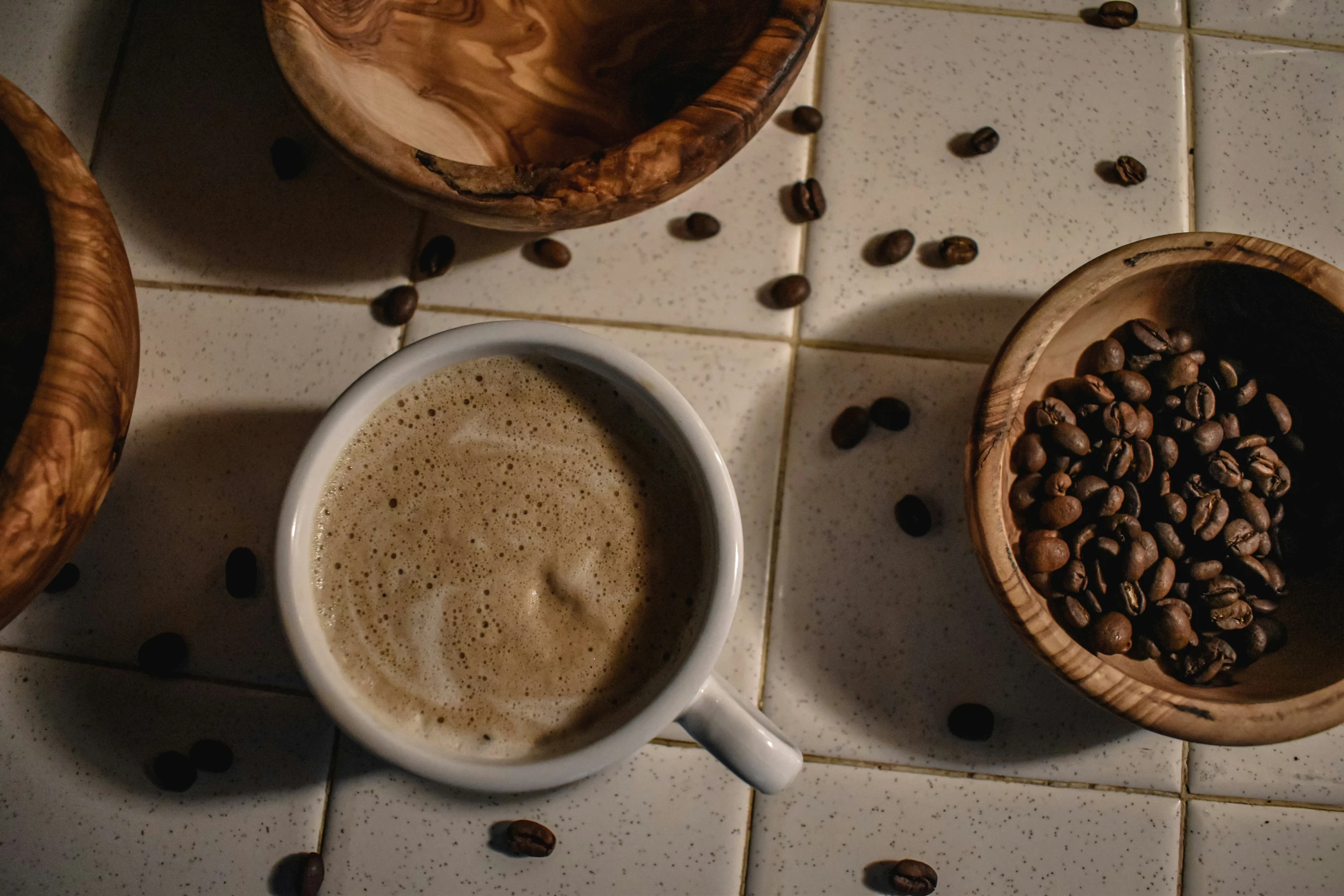 two coffee mugs on a tile counter next to bowls with beans