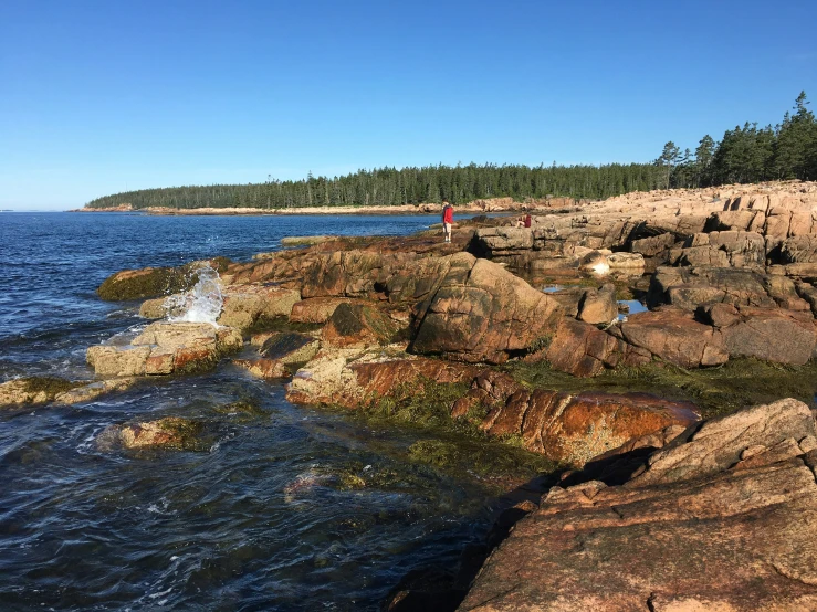 people sit at the edge of a river near a rocky shore