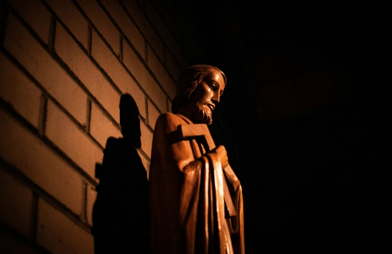 a wooden statue of jesus casting his shadow on the side of a building