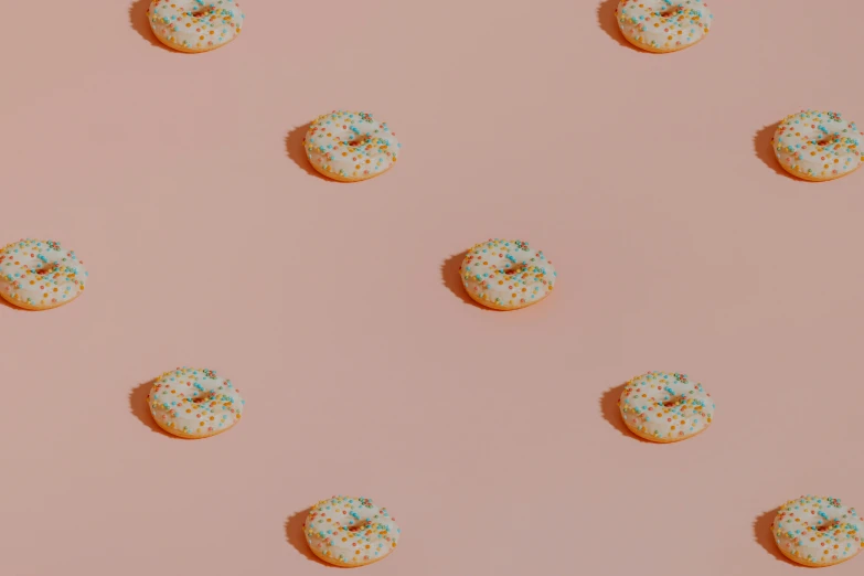 round donuts with green sprinkles and white sprinkles scattered around them on a pink surface