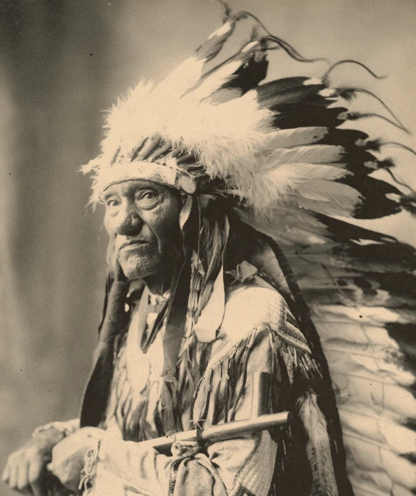 an old po of a native american man wearing feathers and holding a stick