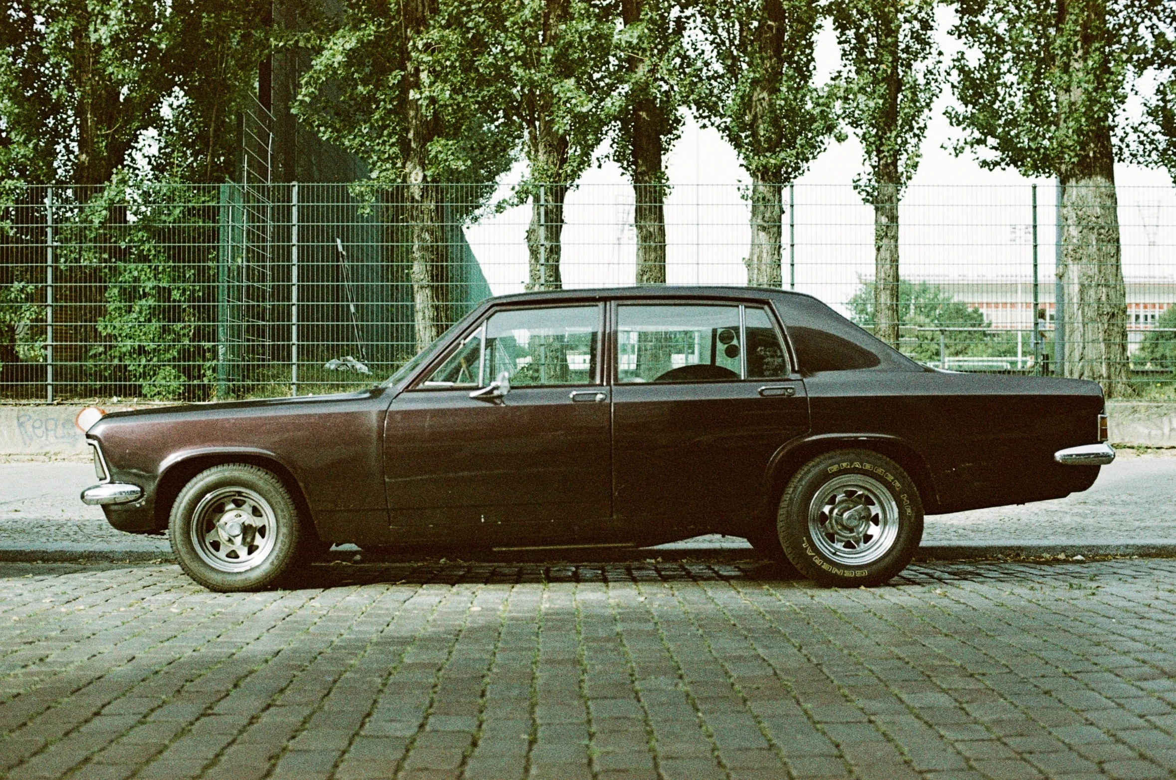 an old style car sits on a brick road in front of a fence